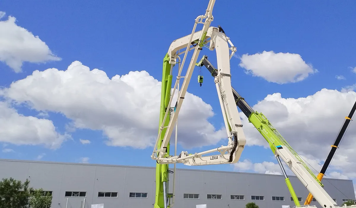 The boom of a concrete pump truck and the boom of a crane are both deployed.